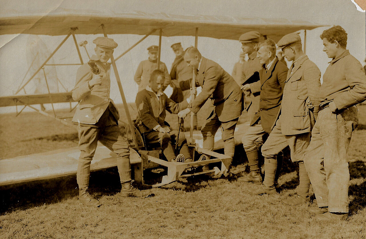 Schwarz-weiß-Foto: Junge sitz in Segelflugzeug und wird von einer Gruppe junger Männer umringt.